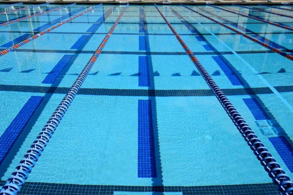 A swimming pool featuring a Cove Blue swimming pool finish, surrounded by lush greenery and a clear blue sky.