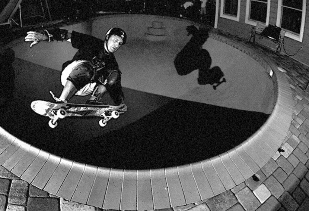 A skateboarder performing a nose grab trick over a swimming pool, showcasing a dynamic swim skate pool design.